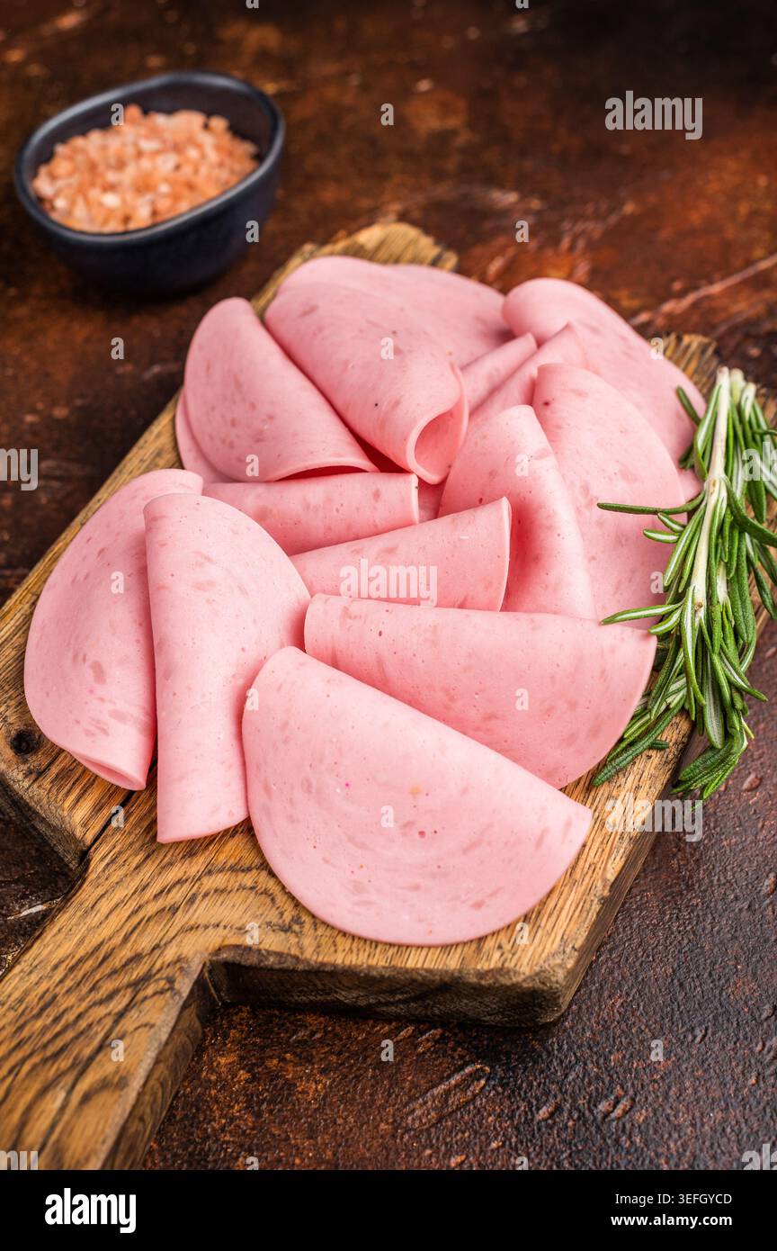 Blick von oben auf Wurst (Mortadella), garniert mit Rosmarin auf einem Schneidebrett. Gourmet-Deli-Konzept auf sattem, dunklem Hintergrund Stockfoto