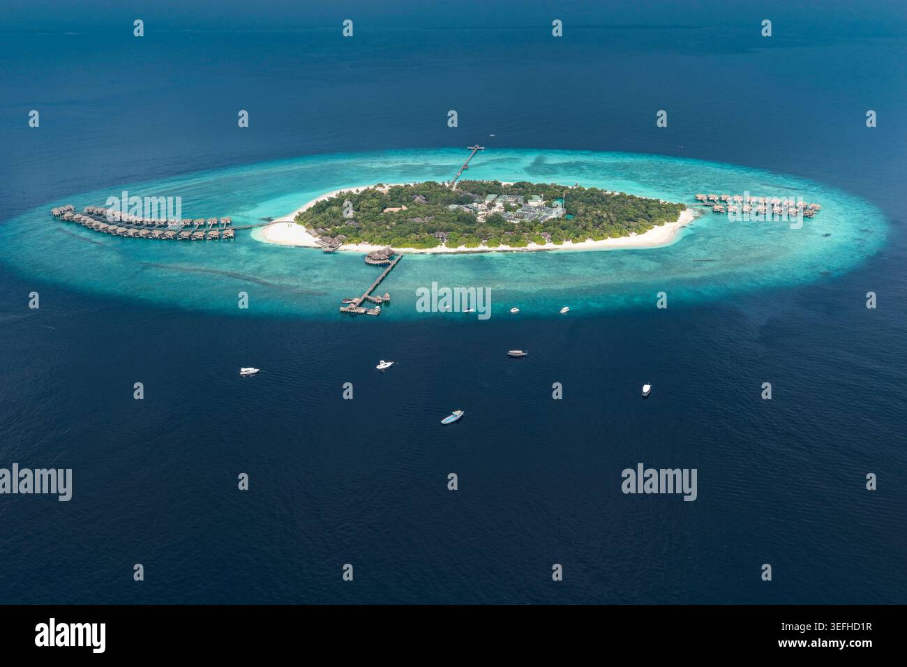 Blick aus der Vogelperspektive auf ein tropisches Inselresort mit Bungalows über dem Wasser, üppiger Vegetation und türkisfarbenen Korallenriffen umgeben von tiefblauem Meereswasser Hoara Stockfoto