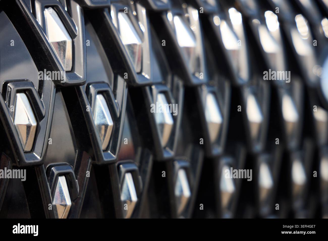 Nahaufnahme des komplexen Kühlergrills des Autos mit sich wiederholenden geometrischen Rautenmustern. Verchromte Elemente stehen im Kontrast zu dunkel strukturiertem B Stockfoto