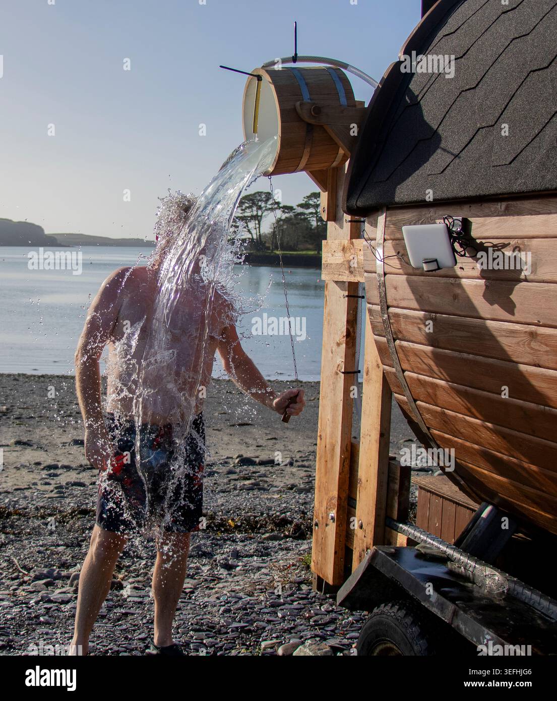 Erwachsener Mann, der eine kalte Dusche nimmt und nach der Sauna einen Eimer mit kaltem Wasser über den Kopf zieht. Stockfoto