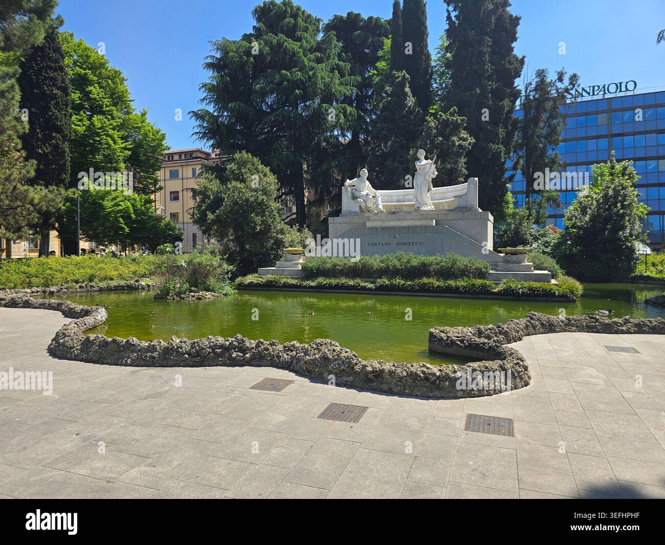 Das Donizetti-Denkmal spiegelt sich im Schwanenteich-Garten der Piazza Cavour, Lower Bergamo, mit dem Teatro Donizetti Beyond, Lombardei, Italien - Smartphone-aufgenommenes Stockfoto