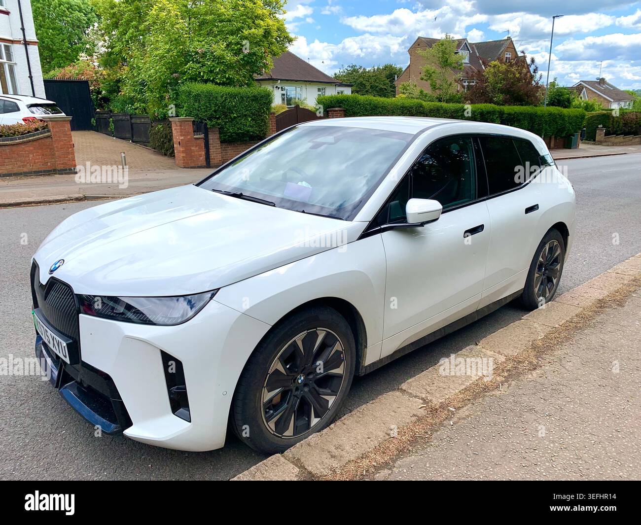 Ein weißer BMW iX Elektro-SUV parkt auf einer ruhigen Wohnstraße in Northamptonshire und präsentiert modernes Design und nachhaltige Vororte - Smartphone-aufgenommenes Stockfoto