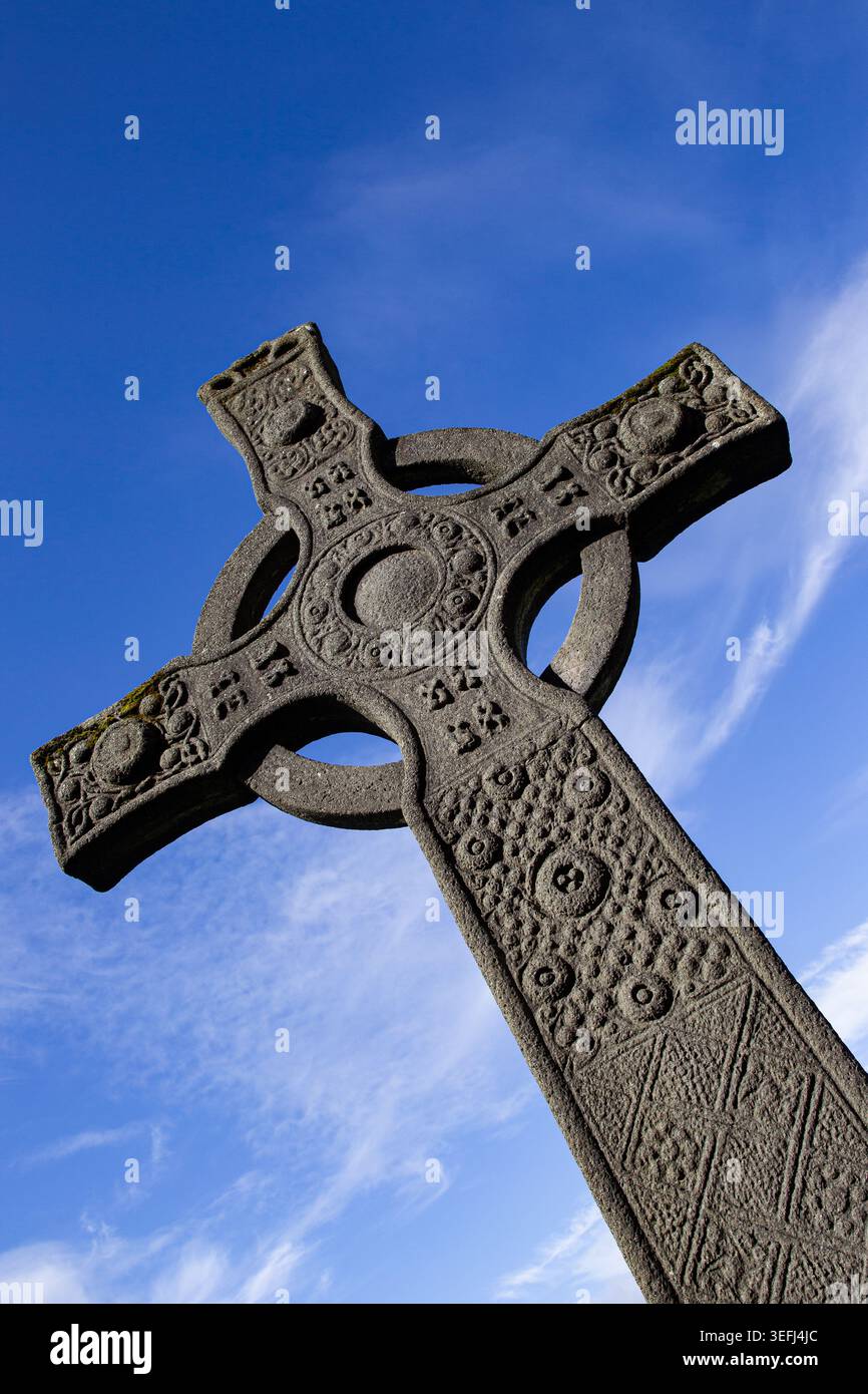Blick auf die komplizierten Schnitzereien auf einem historischen keltischen Steinkreuz in der Iona Abbey unter einem hellblauen Himmel Isle of Iona, Schottland, Großbritannien. Stockfoto