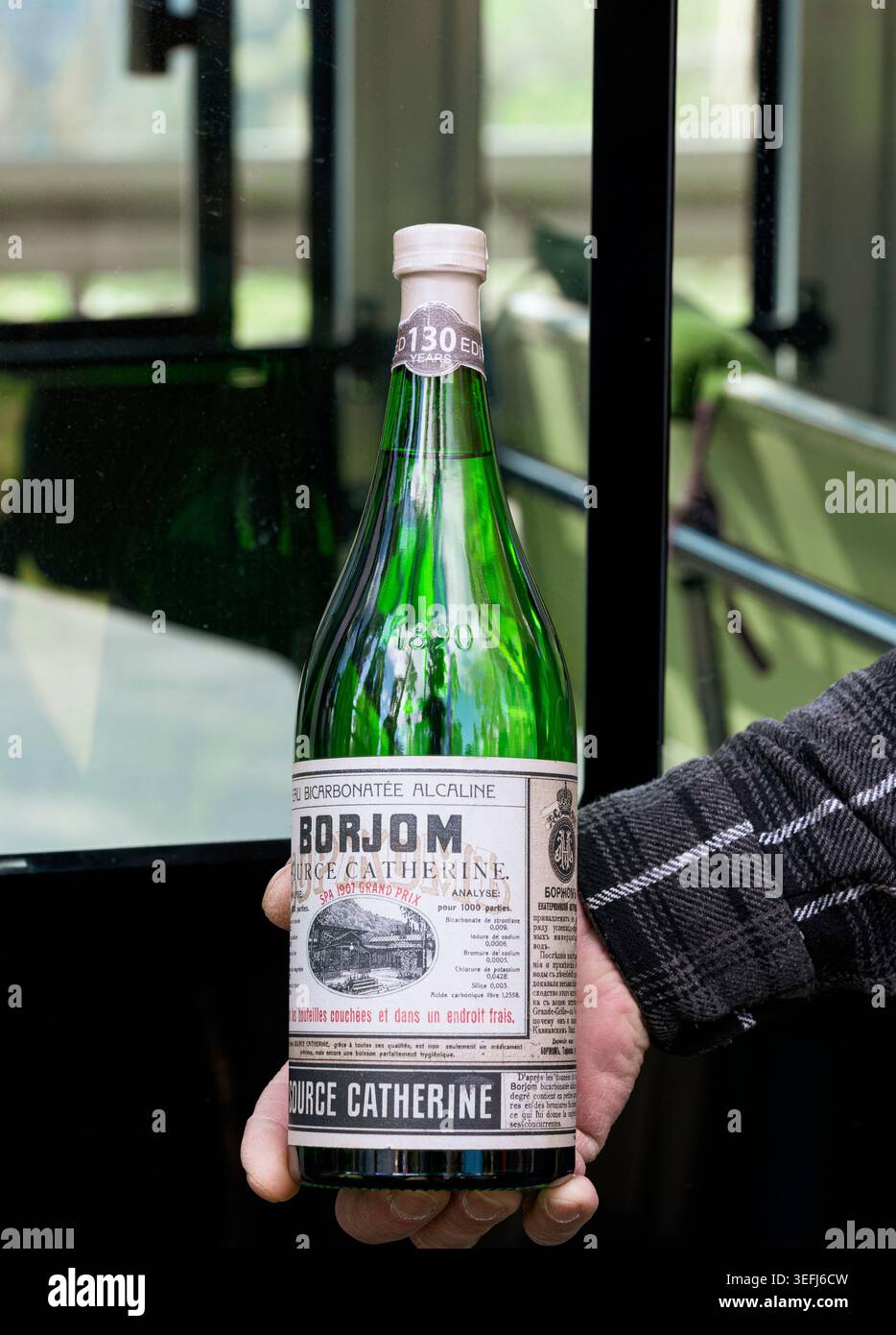 Hand hält die berühmte Borjomi georgianische Mineralwasserflasche aus grünem Glas mit Vintage-Etikett, Ausgabe zum 130. Jahrestag, Georgia - 28. April 2026. Stockfoto