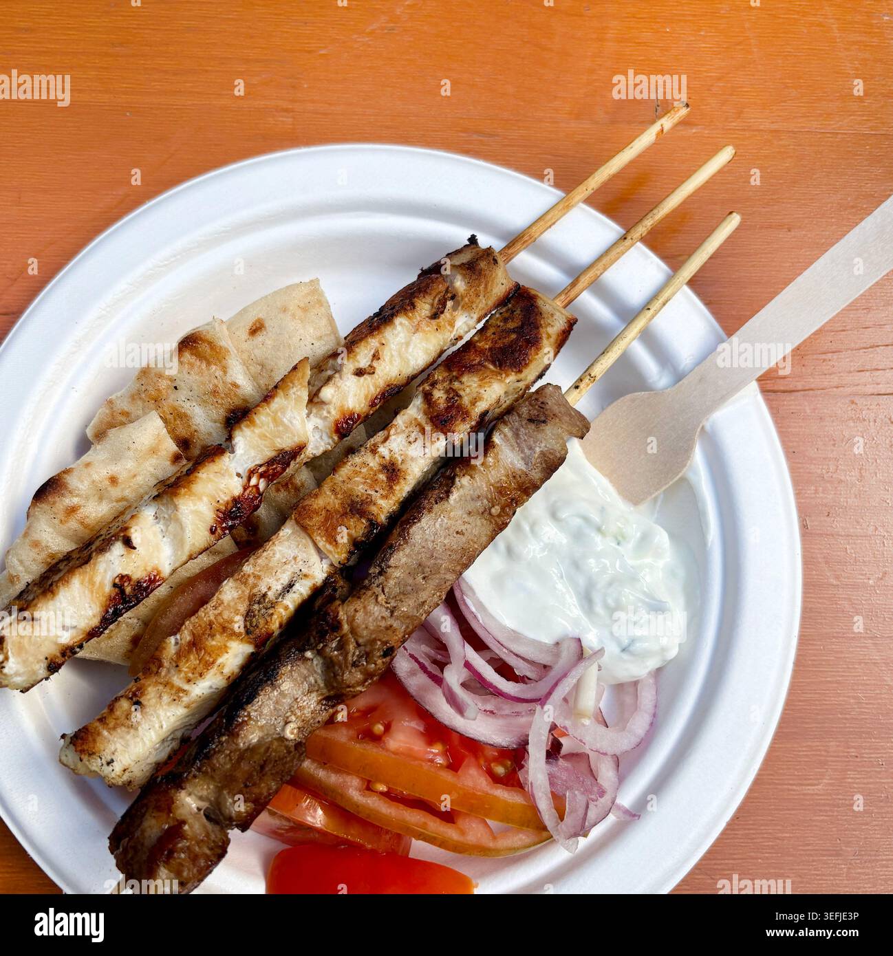 Authentische griechische Essensplatte mit Souvlaki-Spießen, Pitabrot, Tzatziki-Sauce, Tomaten und roten Zwiebeln auf einem Holztisch. Draufsicht. Stockfoto