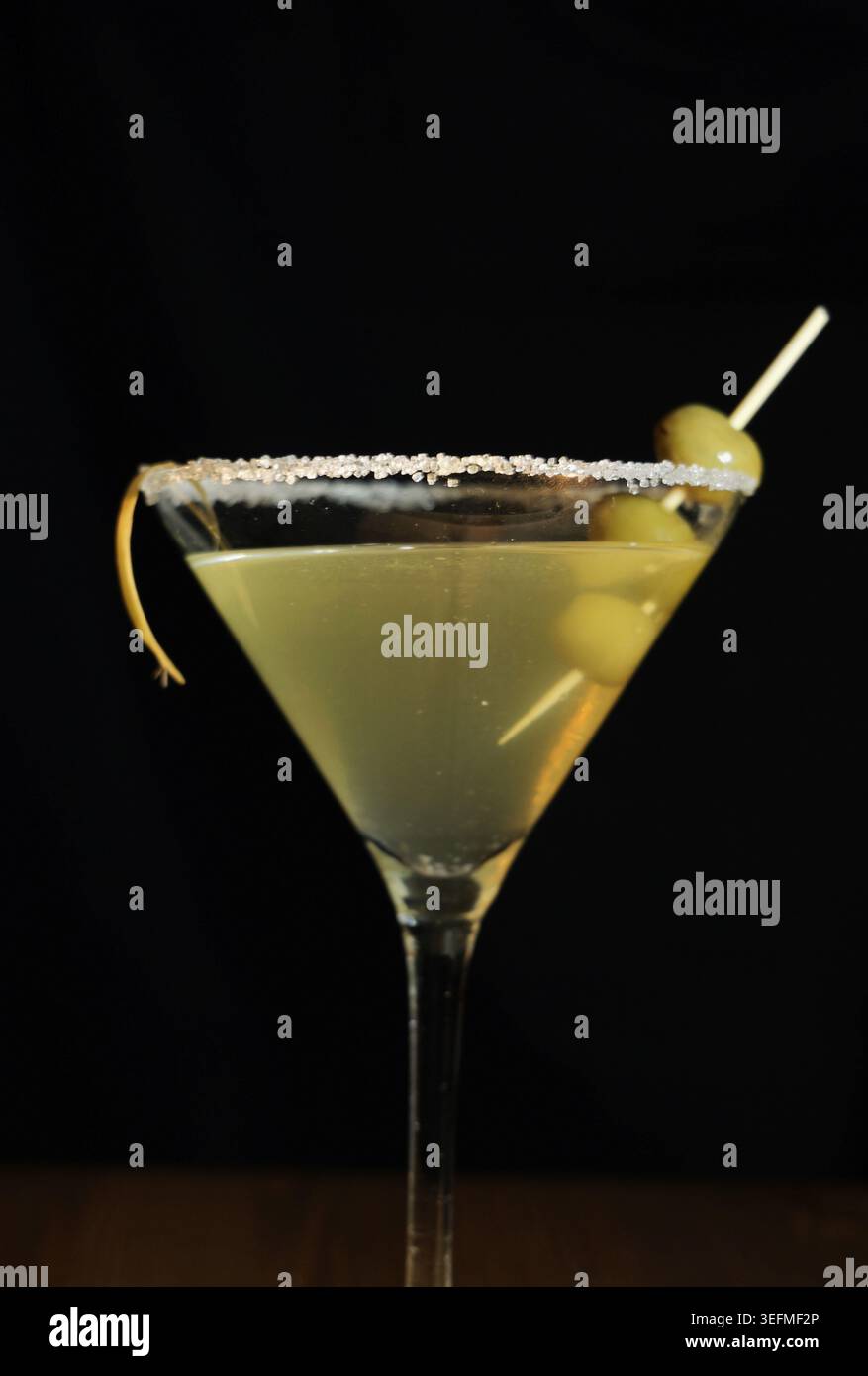 Martini-Cocktail in einem gekühlten klaren Glas mit grünen Oliven, Zitronenduft und gesalzenem Zuckerrand auf dunklem Hintergrund, elegantes klassisches Getränk für Nachtleben Stockfoto