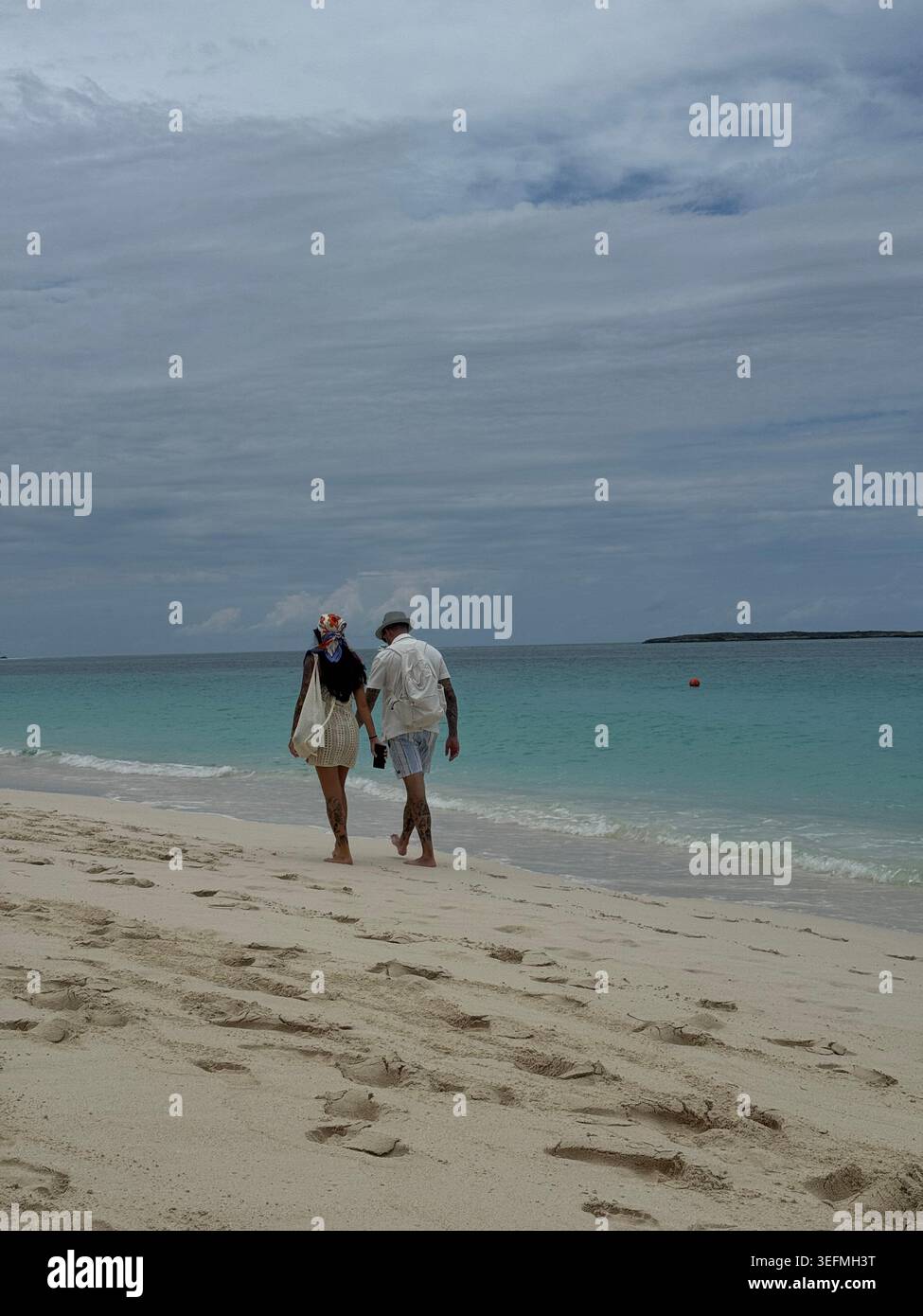 Rückansicht eines romantischen Paares, der Hand in Hand an einem weißen Sandstrand neben dem türkisfarbenen Meer in Nassau, Bahamas, spaziert. - Smartphone-aufgenommenes Stockfoto
