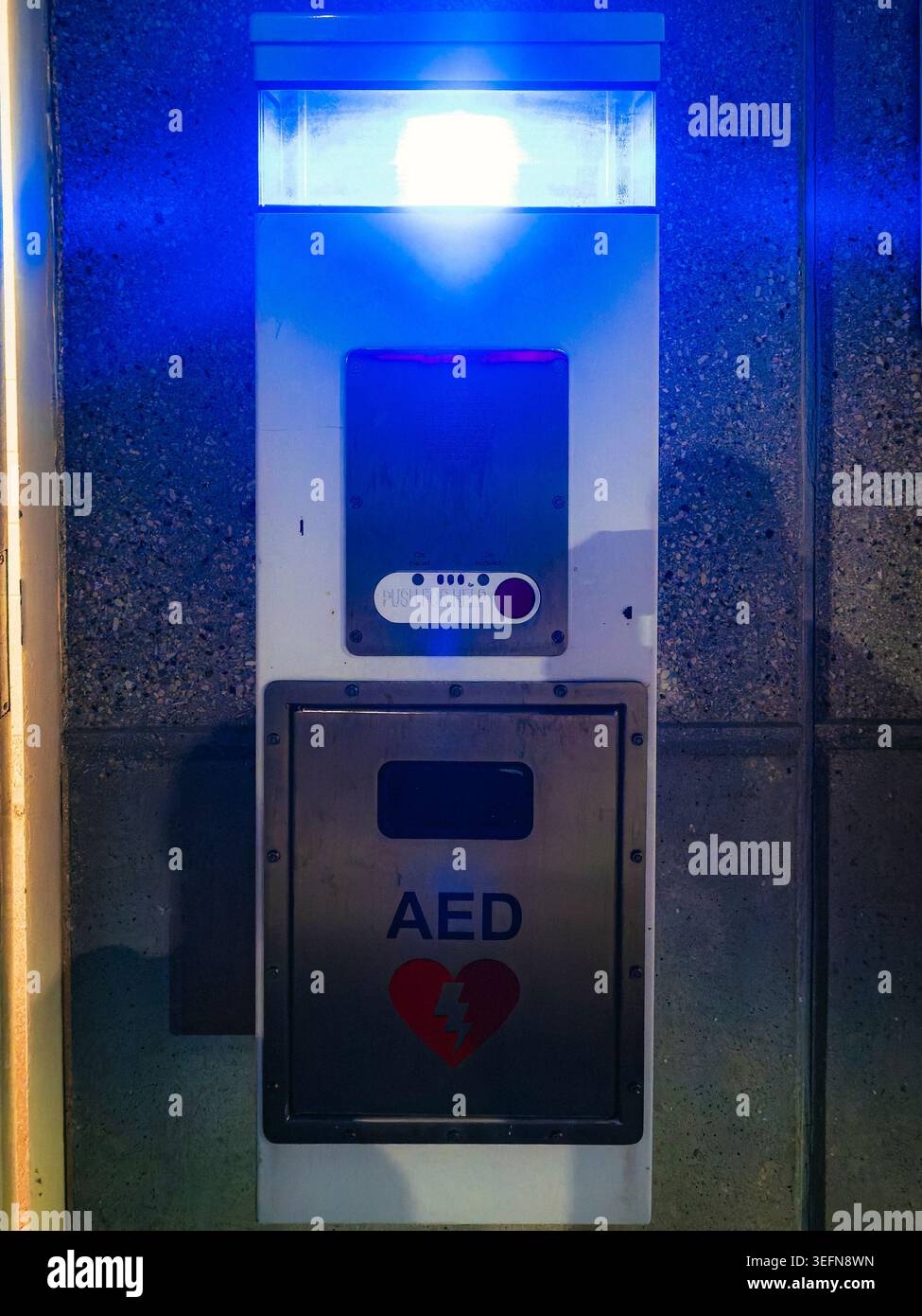 Automatisiertes externes Defibrillatorgerät und eine Notrufzentrale mit leuchtendem blauem Licht auf einer Wandplatte aus strukturiertem Stein Stockfoto