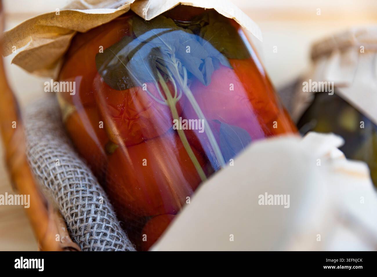 Hausgemachte Dosentomaten mit Basilikumblättern in rustikalem Glaskonservierungsglas Stockfoto