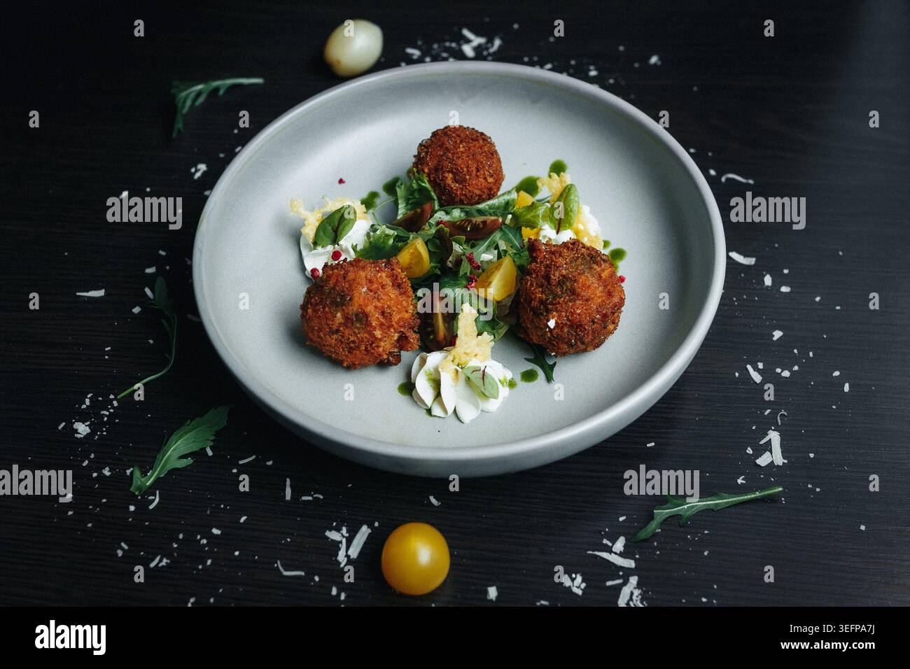 Frittierte Fleischbällchen mit Kräutern und Kirschtomaten auf einem minimalistischen Teller Stockfoto