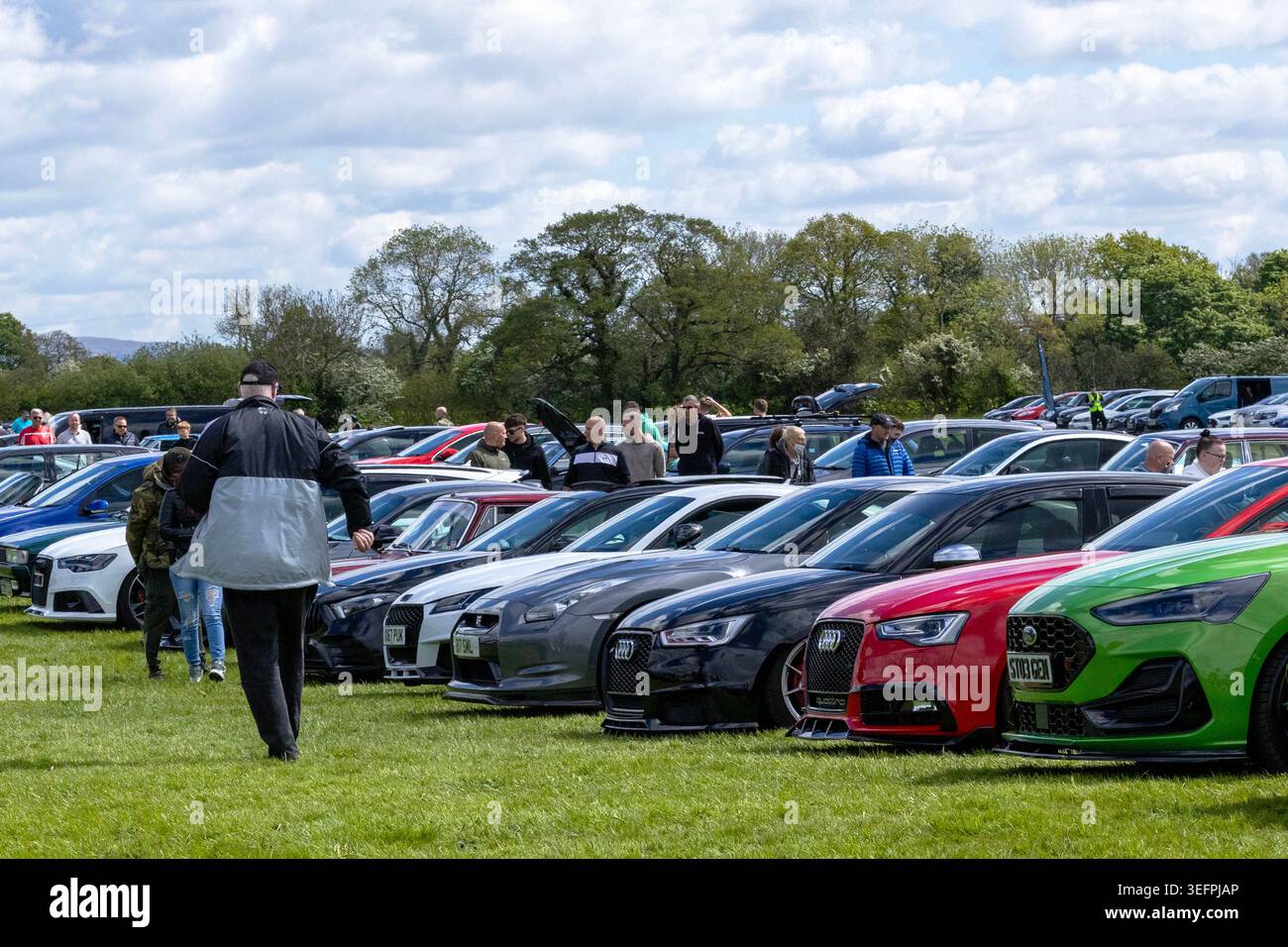 Eine Reihe moderner Sportwagen, darunter ein hellgrüner Ford Focus ST, ein roter Audi und ein grauer Nissan GT-R, alle aufgereiht, damit Zuschauer sie betrachten können. Stockfoto