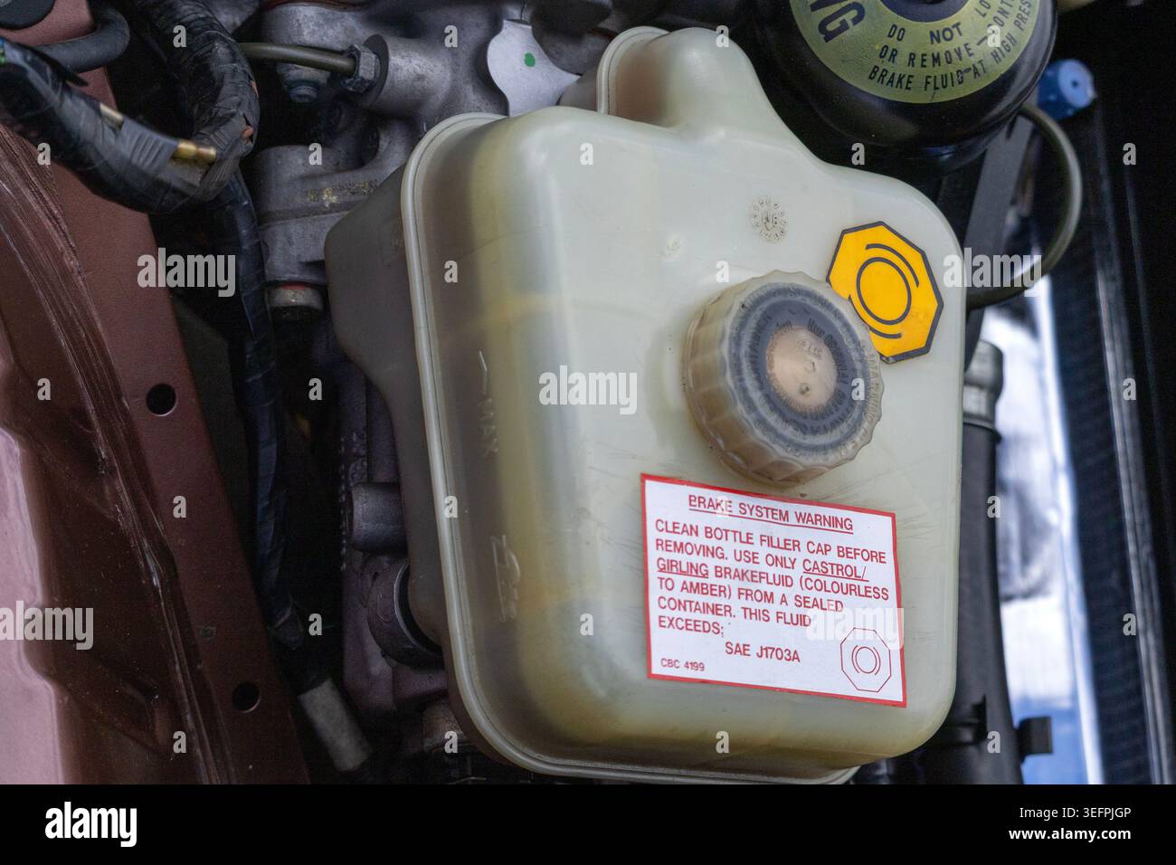 Eine weiße Kunststoff-Bremseflüssigkeitsbehälterflasche mit einem Original-Warnetikett des Fabrikbremssystems. Stockfoto