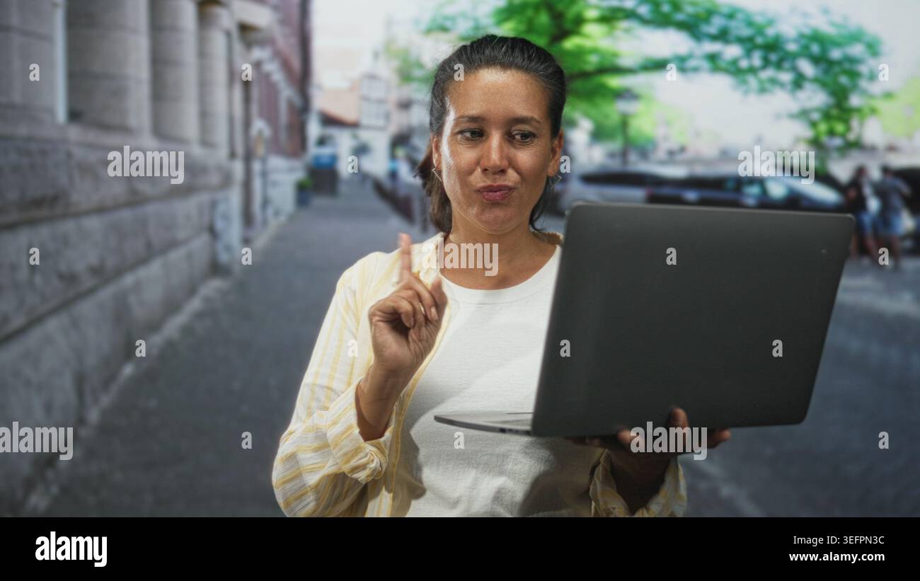 Eine Frau, die den Laptop hält, zeigt den Zeigefinger auf eine urbane Straße, während sie auf den Bildschirm blickt; zielgerichtete Anleitung. Stockfoto