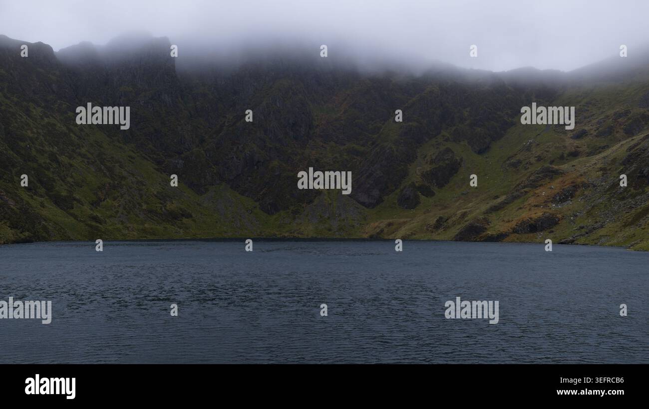 Bergsee umgeben von zerklüfteten Gipfeln und nebeligen Wolken Stockfoto