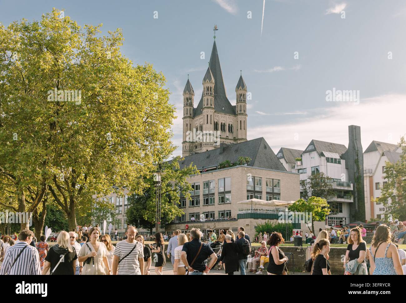 Passanten spazieren an einem sonnigen Sommertag entlang der Großen St. Martin-Kirche Kölns am Ufer des Rheins. Stockfoto