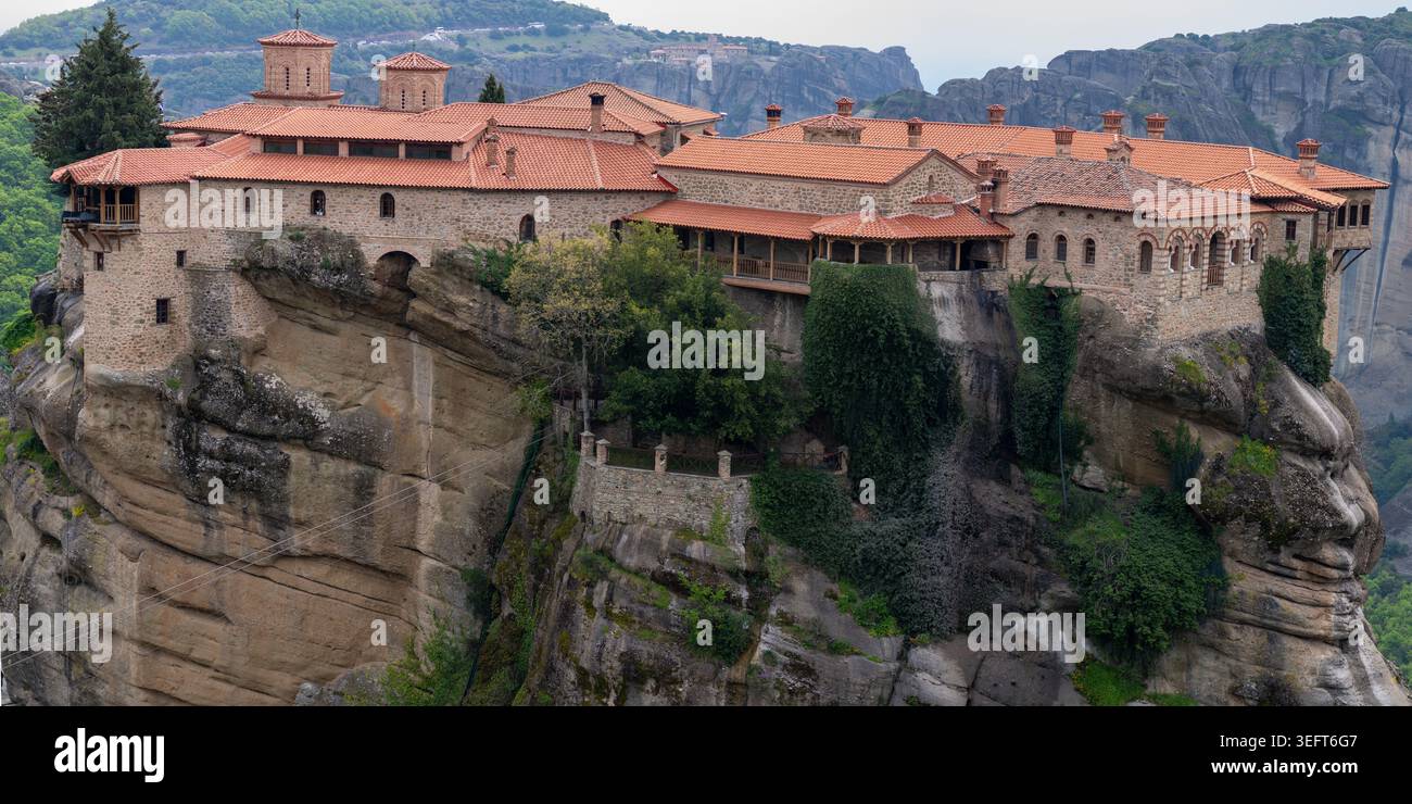 Breiter Panoramablick auf das Kloster Varlaam, das auf einer massiven Klippe thront, mit seinem einzigartigen Steinmauerwerk und den rot gekachelten byzantinischen Dächern. Stockfoto