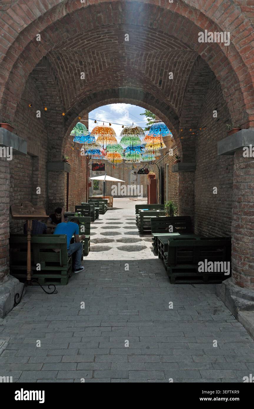 Gemütliches Outdoor Cafe unter Brick Arch und hängende Regenschirme in Shardeni Street Tiflis Georgia vertikale Aussicht Stockfoto