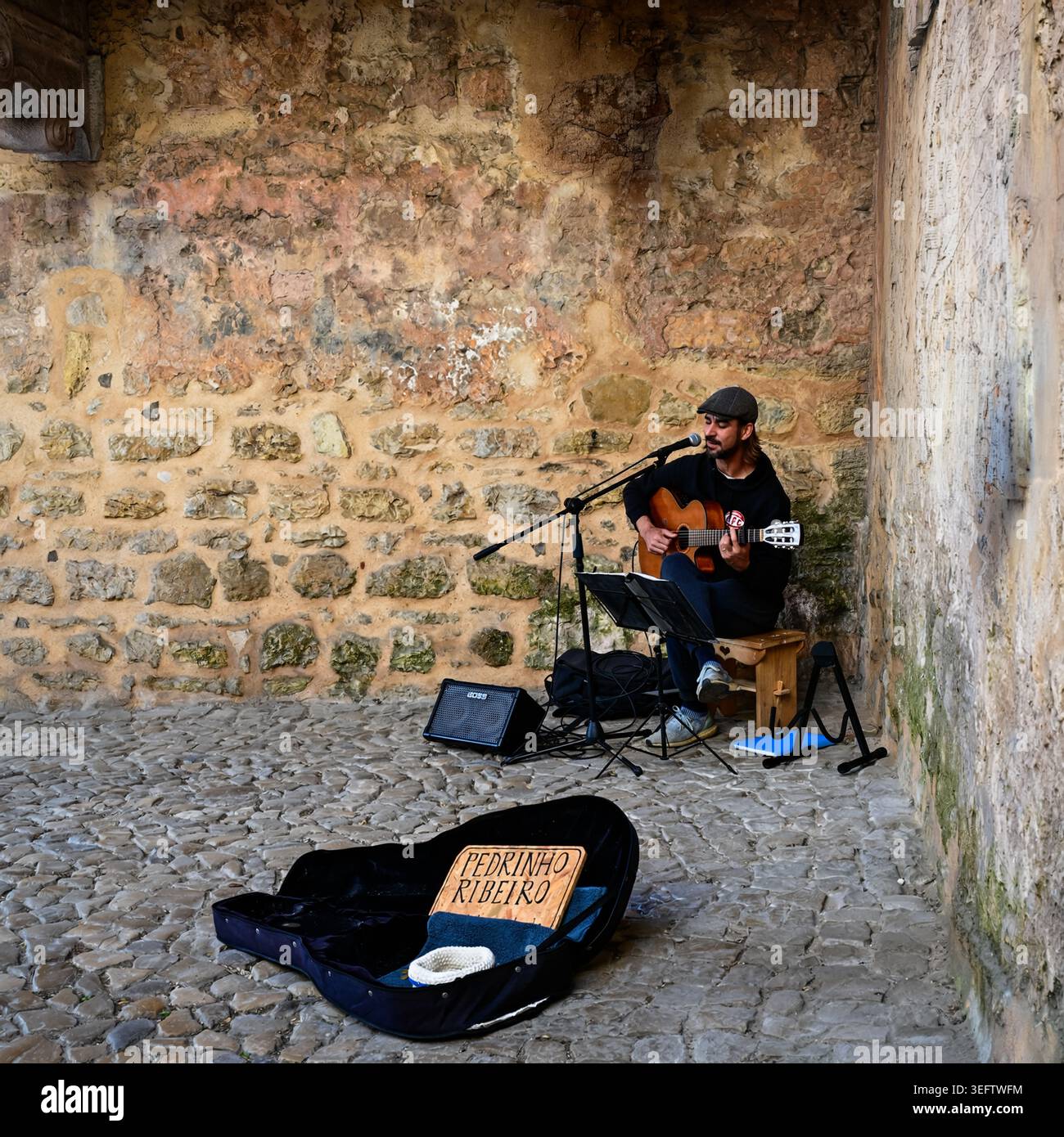 Ein talentierter Straßenmusiker spielt Akustikgitarre in einem rustikalen Innenhof, der eine intime und authentische europäische Atmosphäre schafft. Stockfoto