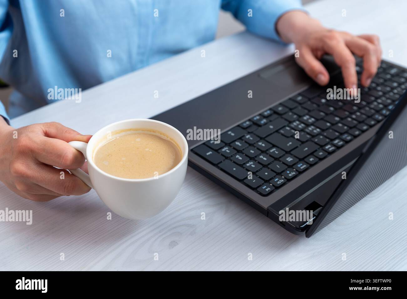 Frau, die an einem Laptop arbeitet und gleichzeitig eine Kaffeetasse in der Hand hält, zeigt produktives Arbeiten an entfernten Standorten und einen komfortablen digitalen Lebensstil Stockfoto