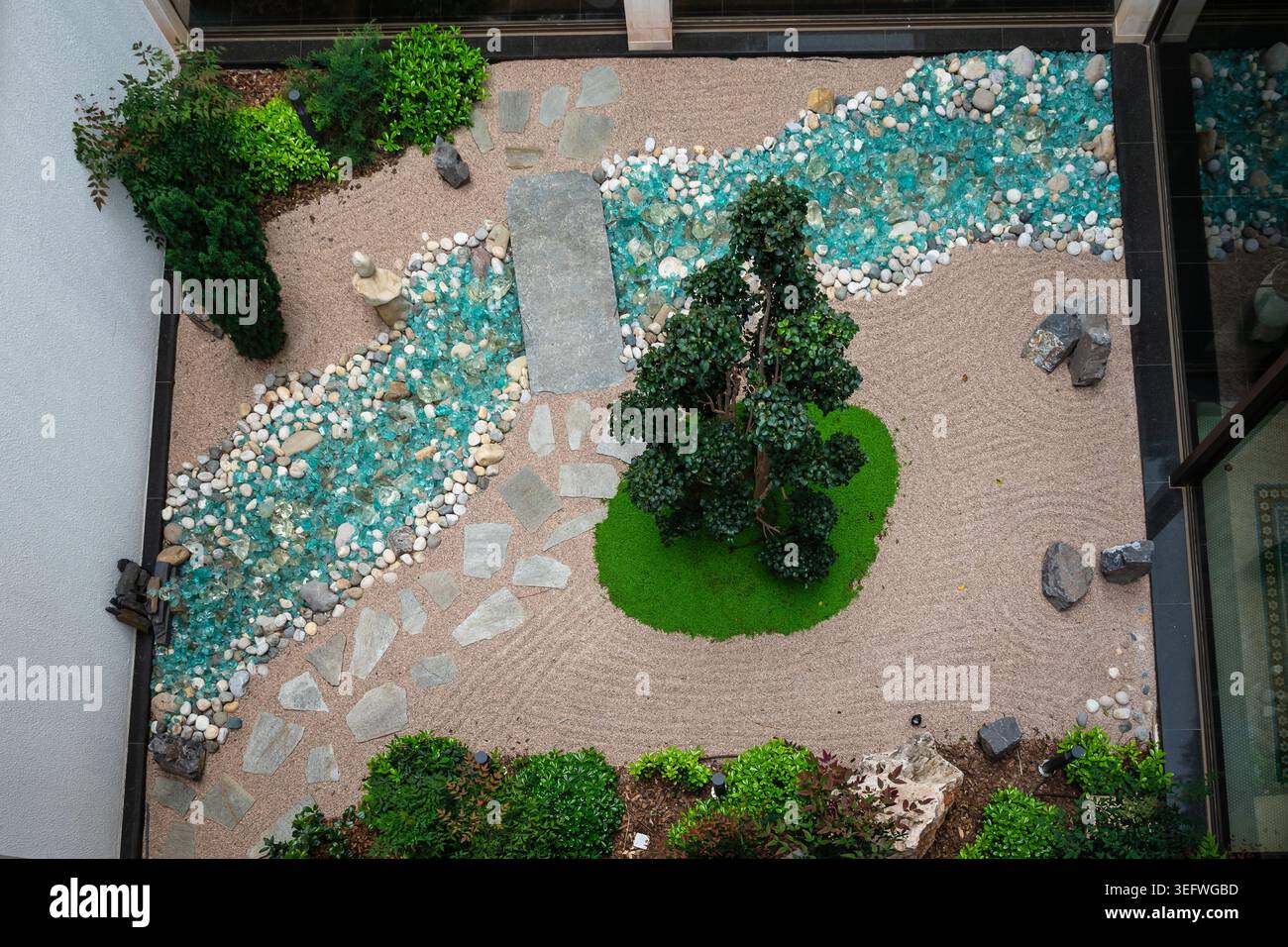 Blick von oben auf einen modernen japanischen Zen-Garten-Innenhof mit hartem Sand und einem Kunstglasbach. Ruhiges, minimalistisches Design Stockfoto