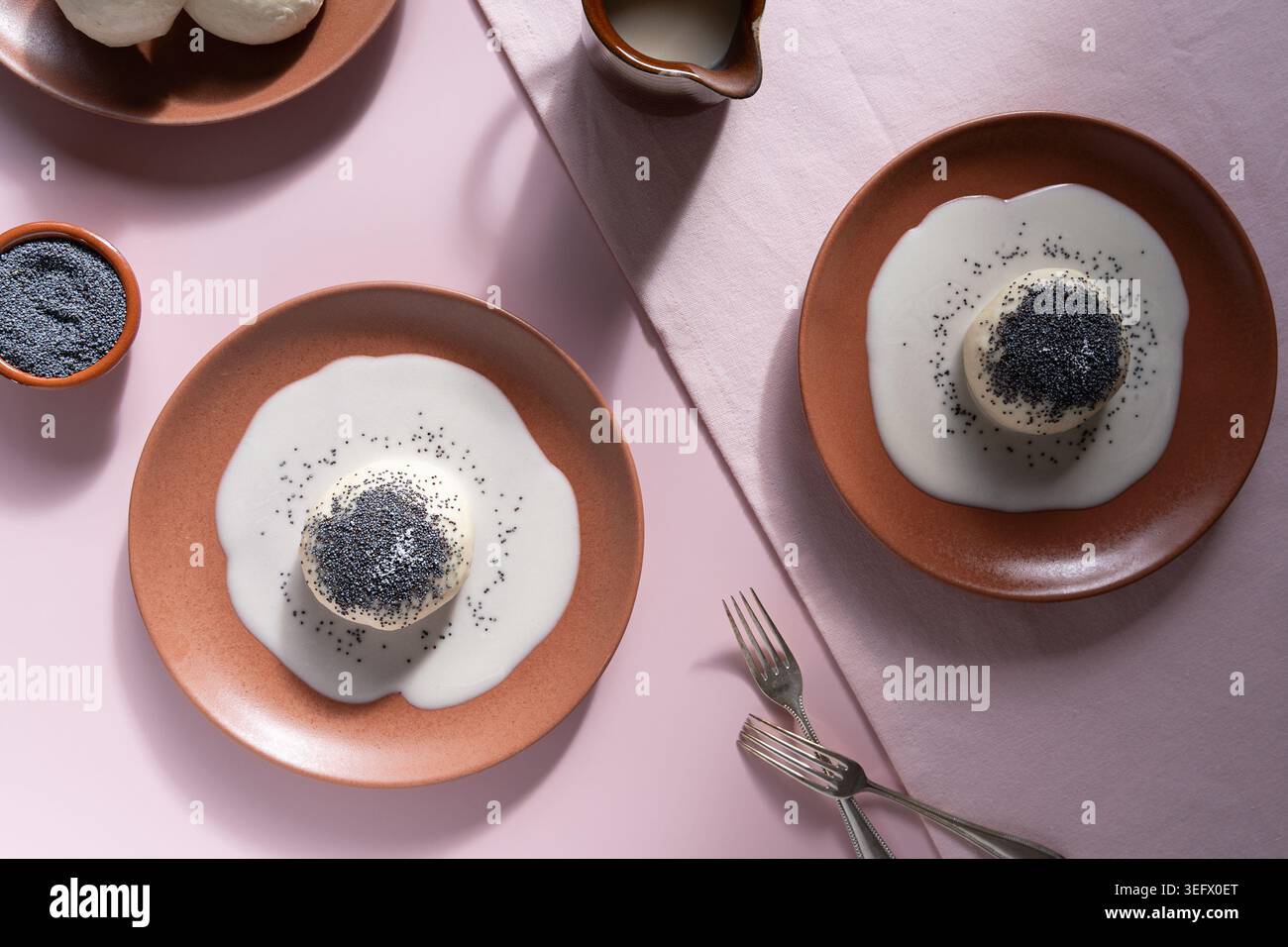 Blick von oben auf deutsche Knödeldesserts mit Creme- und Mohnsamen auf pastellrosa Oberfläche Stockfoto