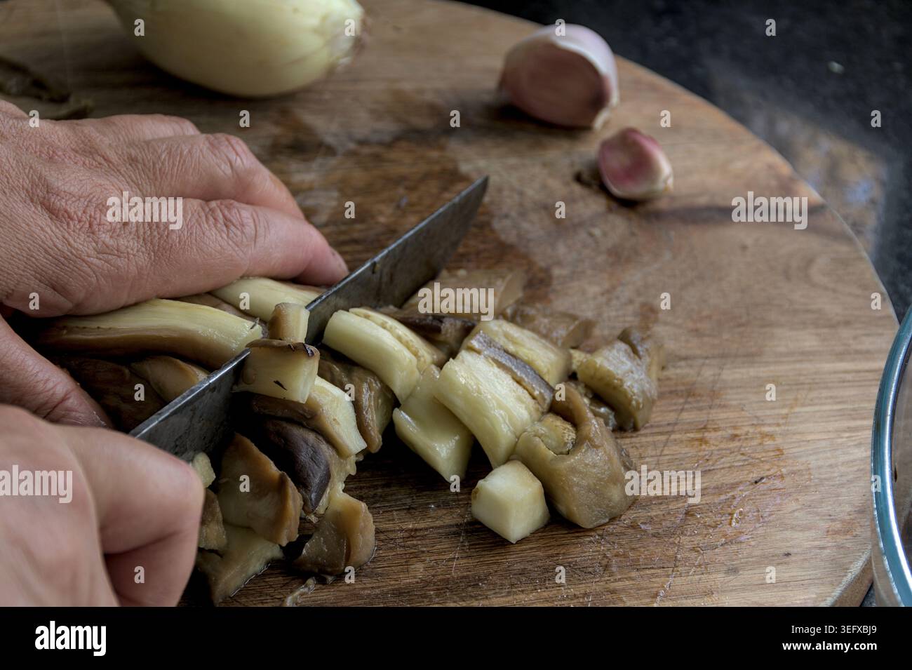 Hacken Sie geröstete Auberginen auf einem Holzschneidebrett mit Knoblauch und Zwiebeln in kleine Stücke. Stockfoto