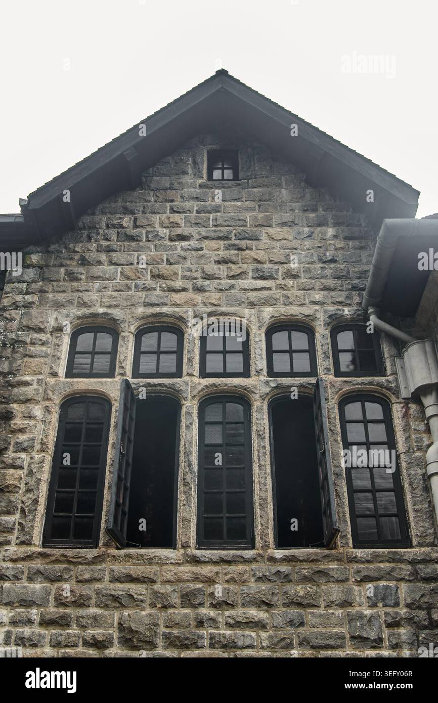 Giebelfassade aus rustikalem Stein mit schwarzen Bogenfenstern, flacher Blick auf alte Wohnimmobilien Stockfoto