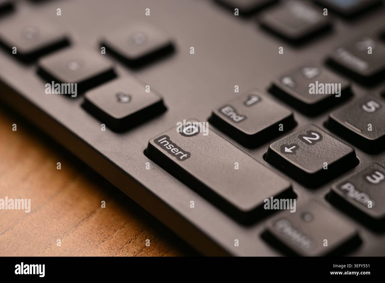Seitlich angewinkelte Draufsicht Makro Nahaufnahme Schwarze Tastatur zur Hervorhebung von Null- und Einfügetasten auf dem numerischen Tastenfeld mit weichem, unscharfem Hintergrund Stockfoto