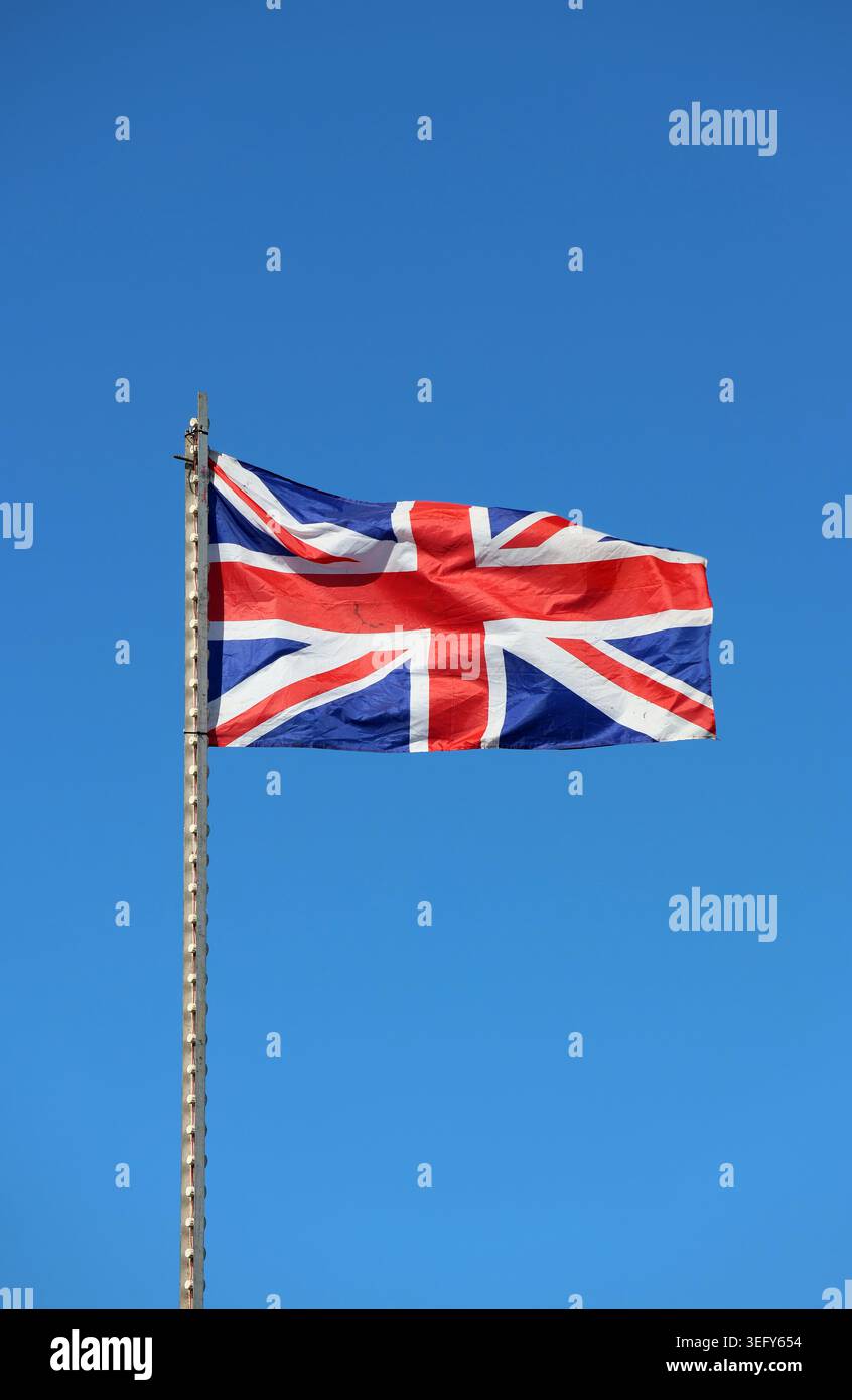 Die Nationalflagge des Vereinigten Königreichs winkt auf einem Fahnenmast vor einem klaren blauen Himmel Stockfoto