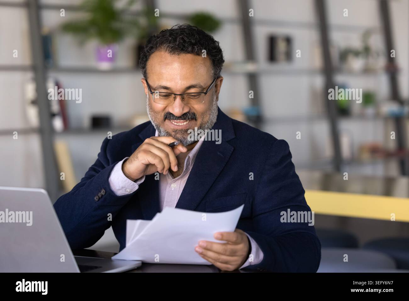 Lächelnder Geschäftsmann mittleren Alters, der Finanzberichte überprüft Stockfoto