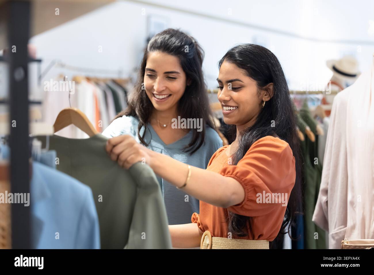 Zwei stilvolle junge Frauen, die in einer modernen Boutique gemeinsam Kleidung auswählen Stockfoto