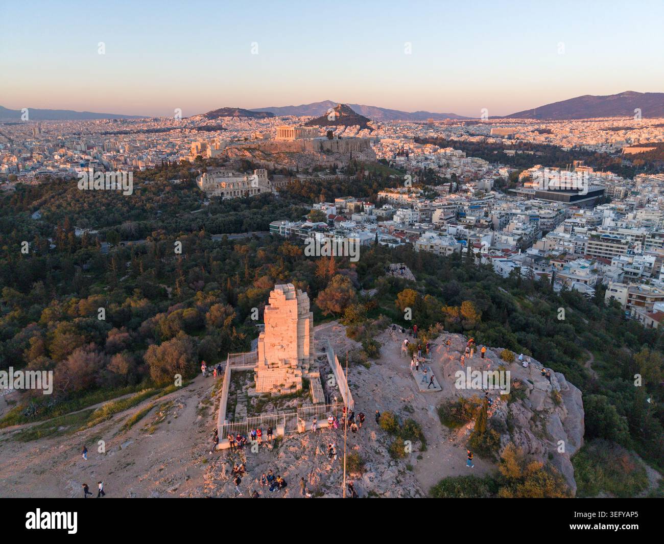 Ein Luftbild des Philopappos Monuments mit Blick auf die Akropolis und den Parthenon während eines goldenen Sonnenuntergangs in Athen, Griechenland. Stockfoto