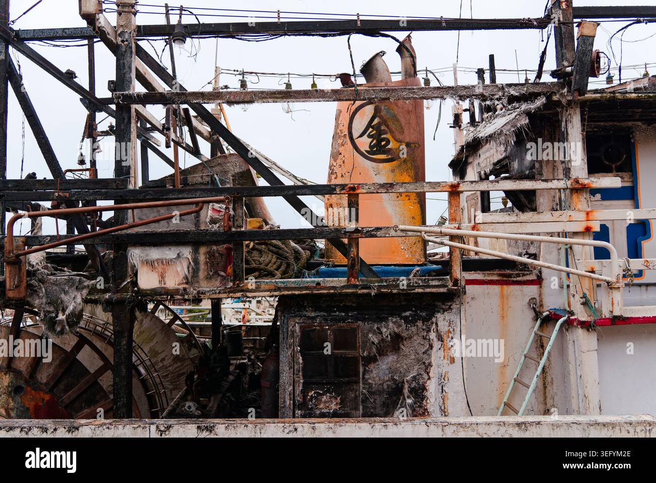 Yilan, Taiwan - 31. März 2025: Feuerhädigter Trawler in Nanfangao mit verkohltem Aufbau, verbrannten Rahmen und rostigen Netzrollen entlang des Rumpfes. Stockfoto