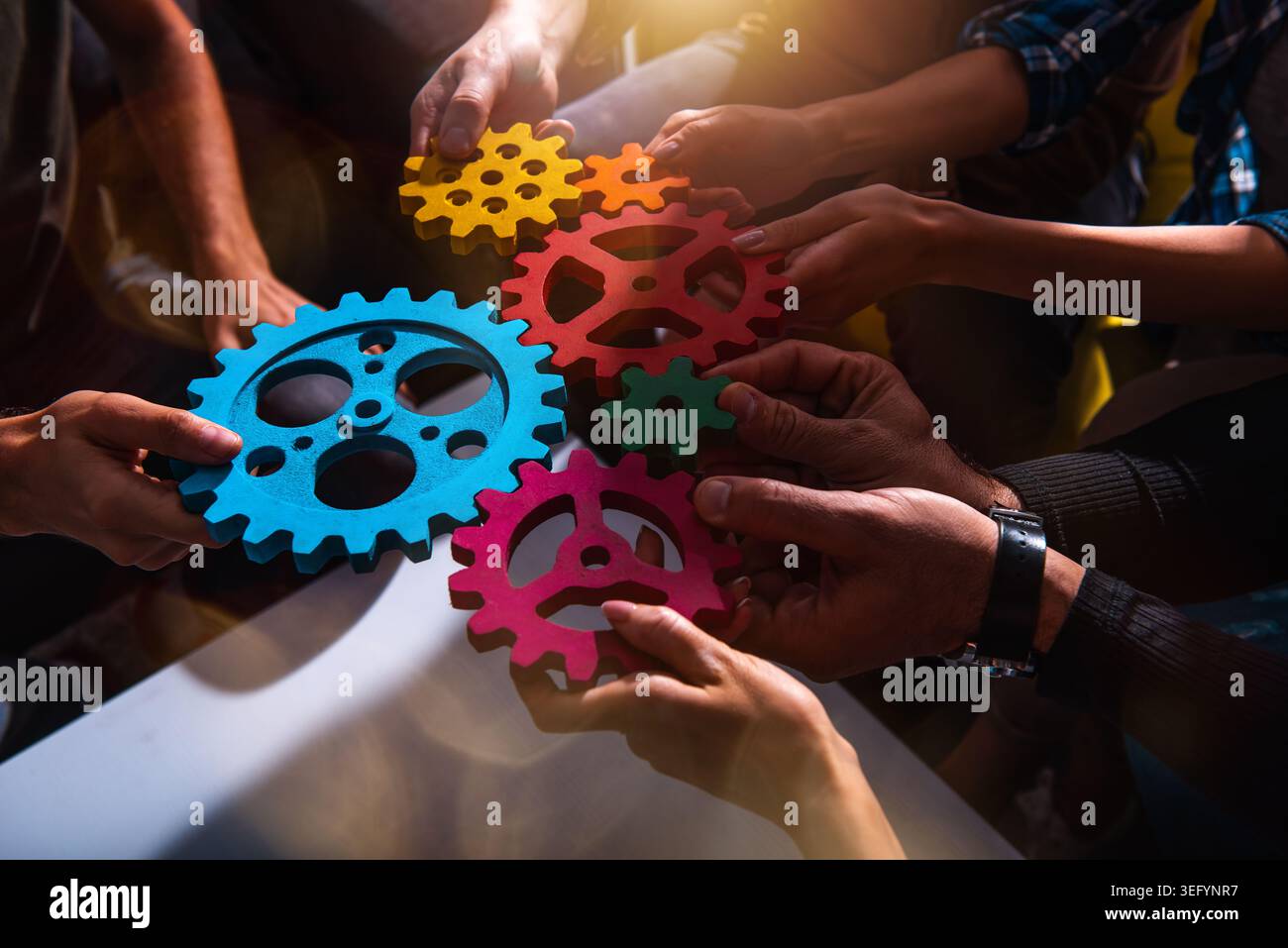 Während eines Gruppenworkshops arbeiten die Hände zusammen, um farbenfrohe Zahnräder in einer kreativen Aktivität miteinander zu verbinden Stockfoto