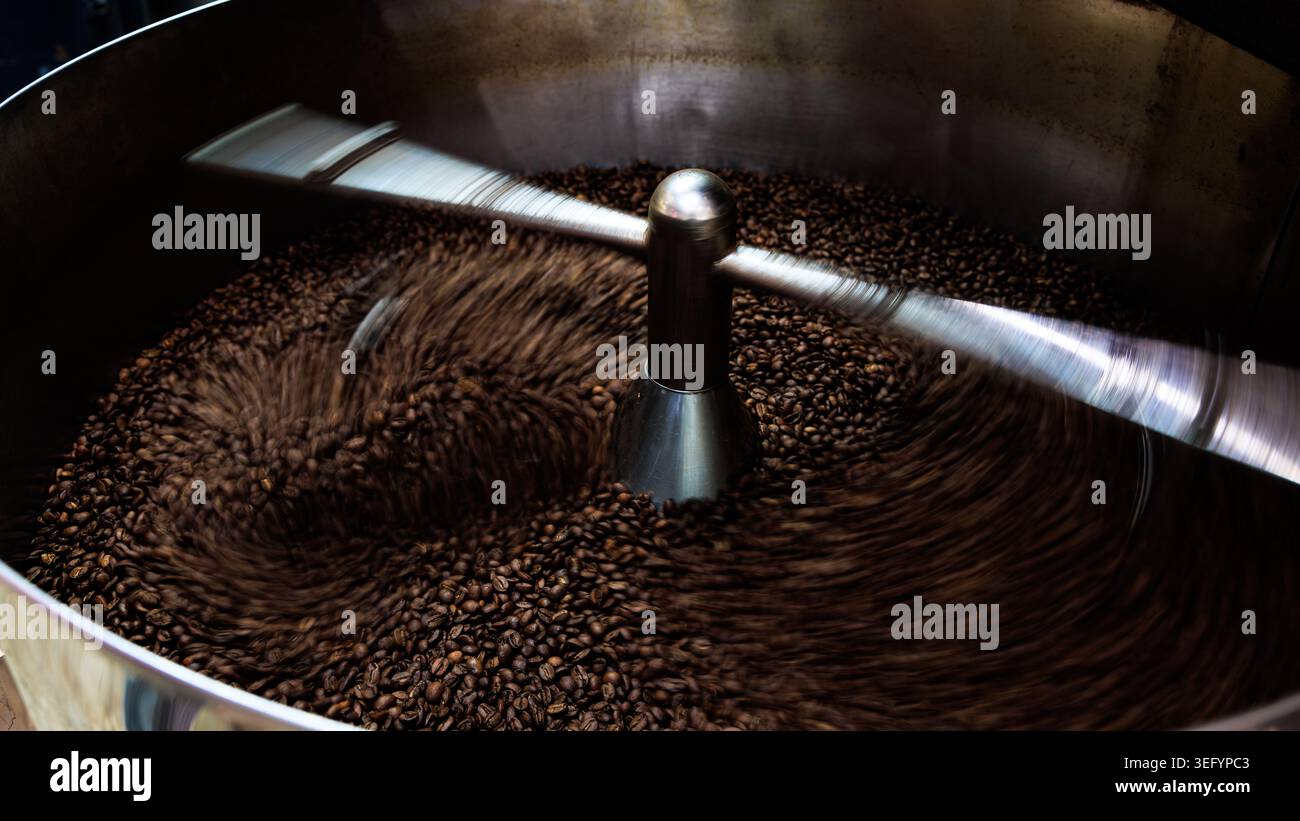 Nahaufnahme einer Kühlschale für industrielle Kaffeeröster mit mechanischen Armen zum Rühren frisch gerösteter Kaffeebohnen während der Produktion. Stockfoto