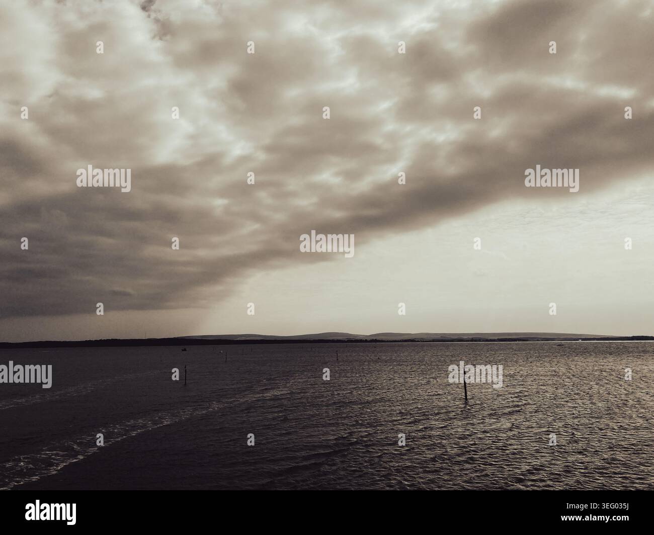 Monochromes Sepia-Bild von dramatischen Wolken über dem Meer an einem ruhigen Sommertag - Smartphone-aufgenommenes Stockfoto