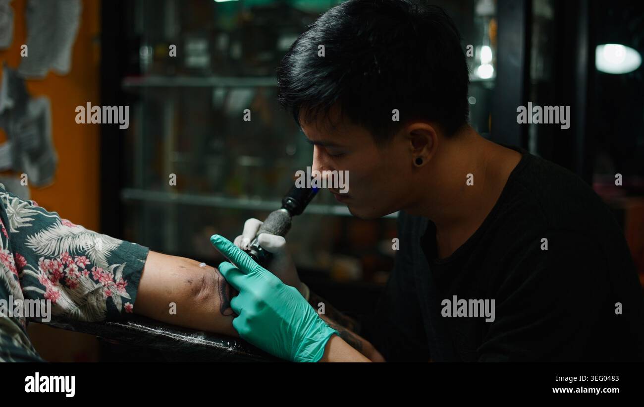Der Tätowierer erstellt sorgfältig ein neues Design auf dem Arm des Kunden mit der Maschine Stockfoto