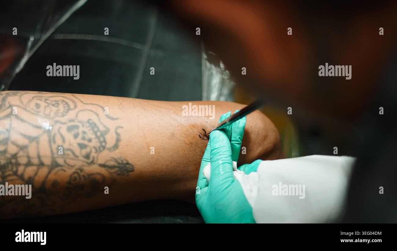 Tätowierende Hand, die kleine Körperkunst mit grünen Handschuhen auf den Arm des Kunden stochst Stockfoto