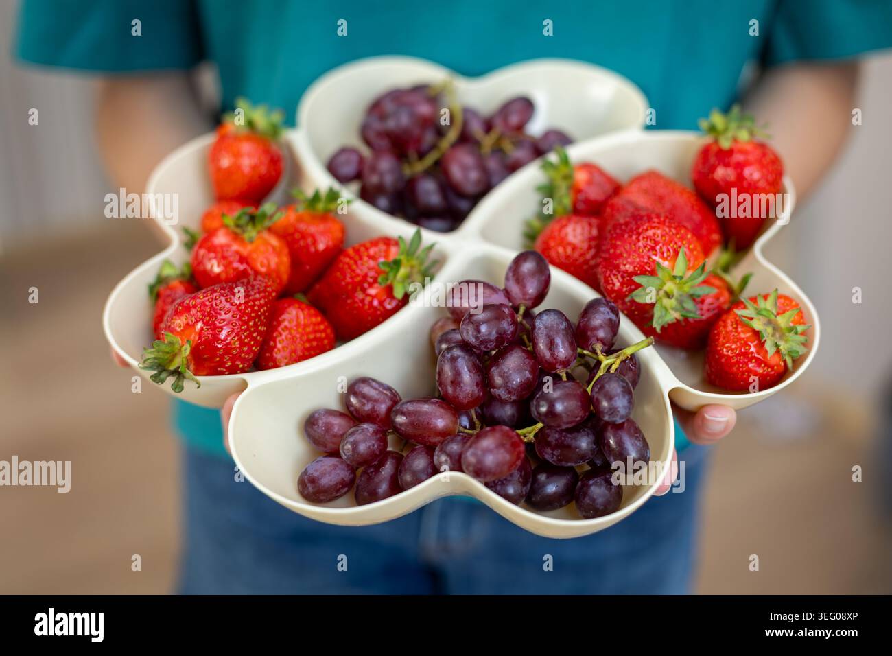 Frische Erdbeeren Und Trauben Im Obsttablett. Person hält ein geteiltes Tablett gefüllt mit Reifen Erdbeeren und roten Trauben für gesunde Ernährung, Party Stockfoto
