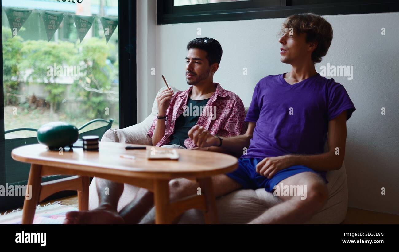 Junge Männer, die sich in der Cannabis Lounge entspannen, einen Joint rauchen und sich unterhalten Stockfoto