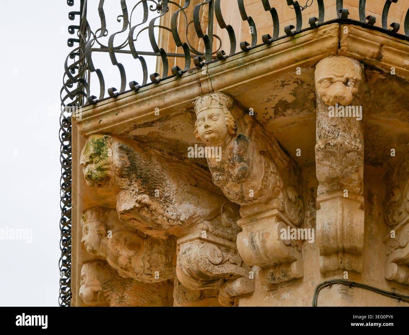 Nahaufnahme eines schönen historischen barocken Steinbalkons mit kunstvoll geschnitzten Gesichtern, mythischen Figuren und einem dunklen schmiedeeisernen Geländer in Europa Stockfoto