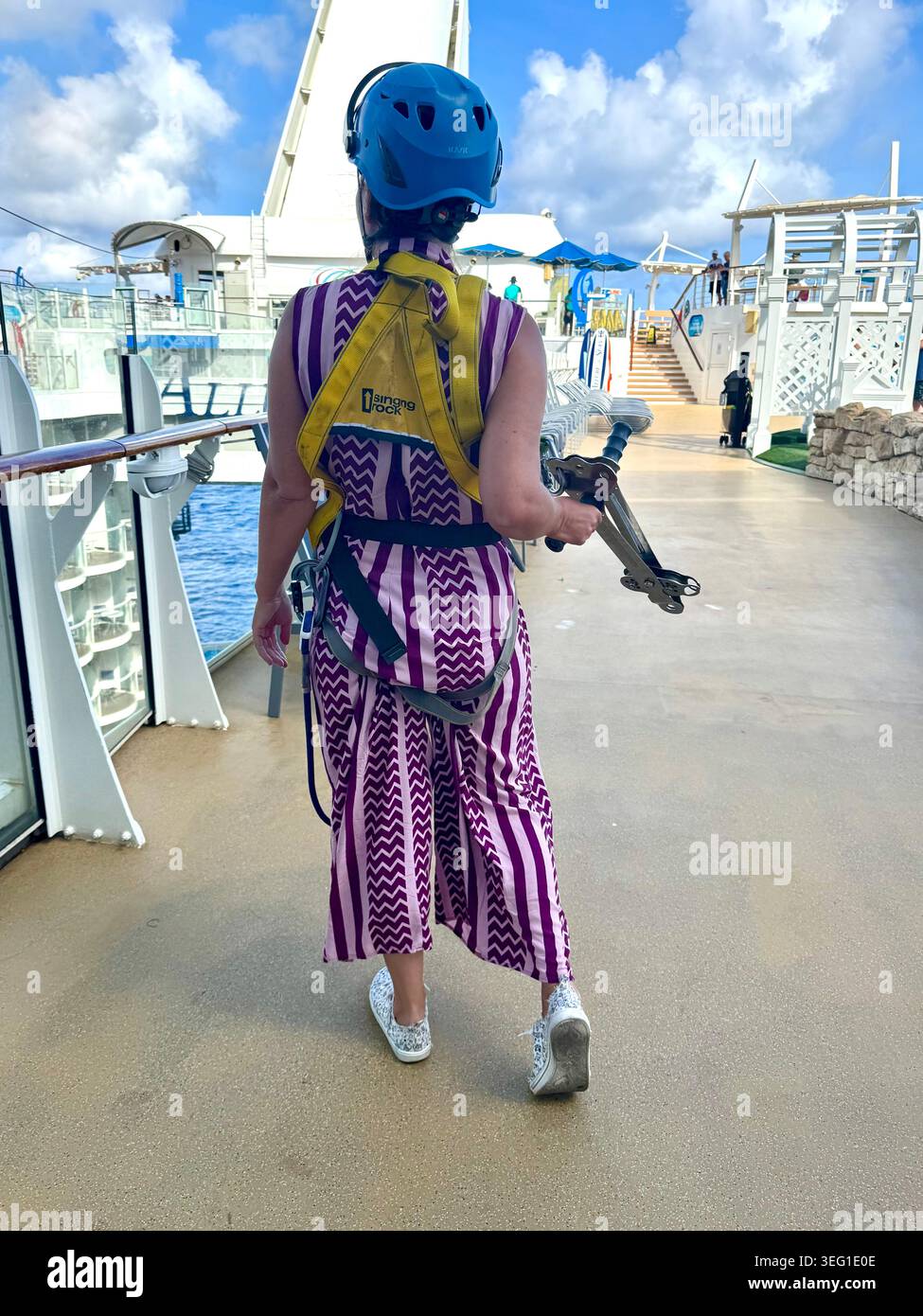 Rückansicht einer Frau mit Sicherheitsgurt, Schwimmweste und Helm, die auf dem oberen Sportdeck eines Kreuzfahrtschiffs läuft. Stockfoto