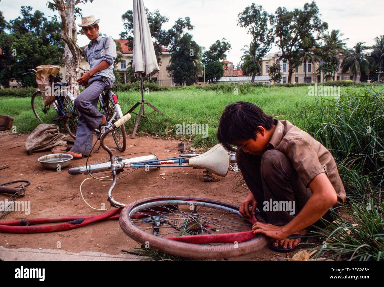 Ein Straßenhändler, der Fahrräder repariert, repariert eine Reifenpanne, Phnom Penh, Kambodscha, 1987 Stockfoto