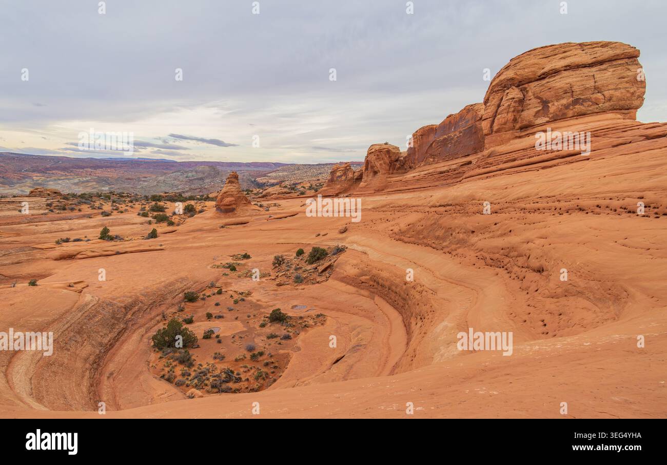 Massive rote Gesteinsschichten kreisen durch einen riesigen Canyon, während verstreute grüne Sträucher auf dem strukturierten Boden des Canyons liegen. Stockfoto