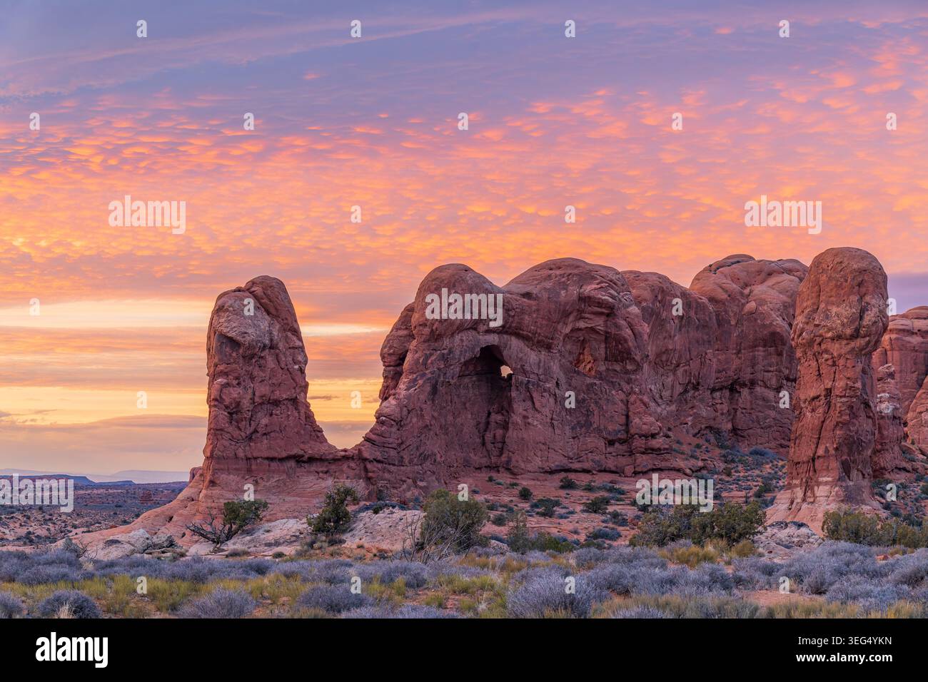 Massive rote Sandsteinbögen stehen inmitten des Sagebrausches, während ein farbenfroher Himmel die Wüstenlandschaft in der Dämmerung erleuchtet Stockfoto
