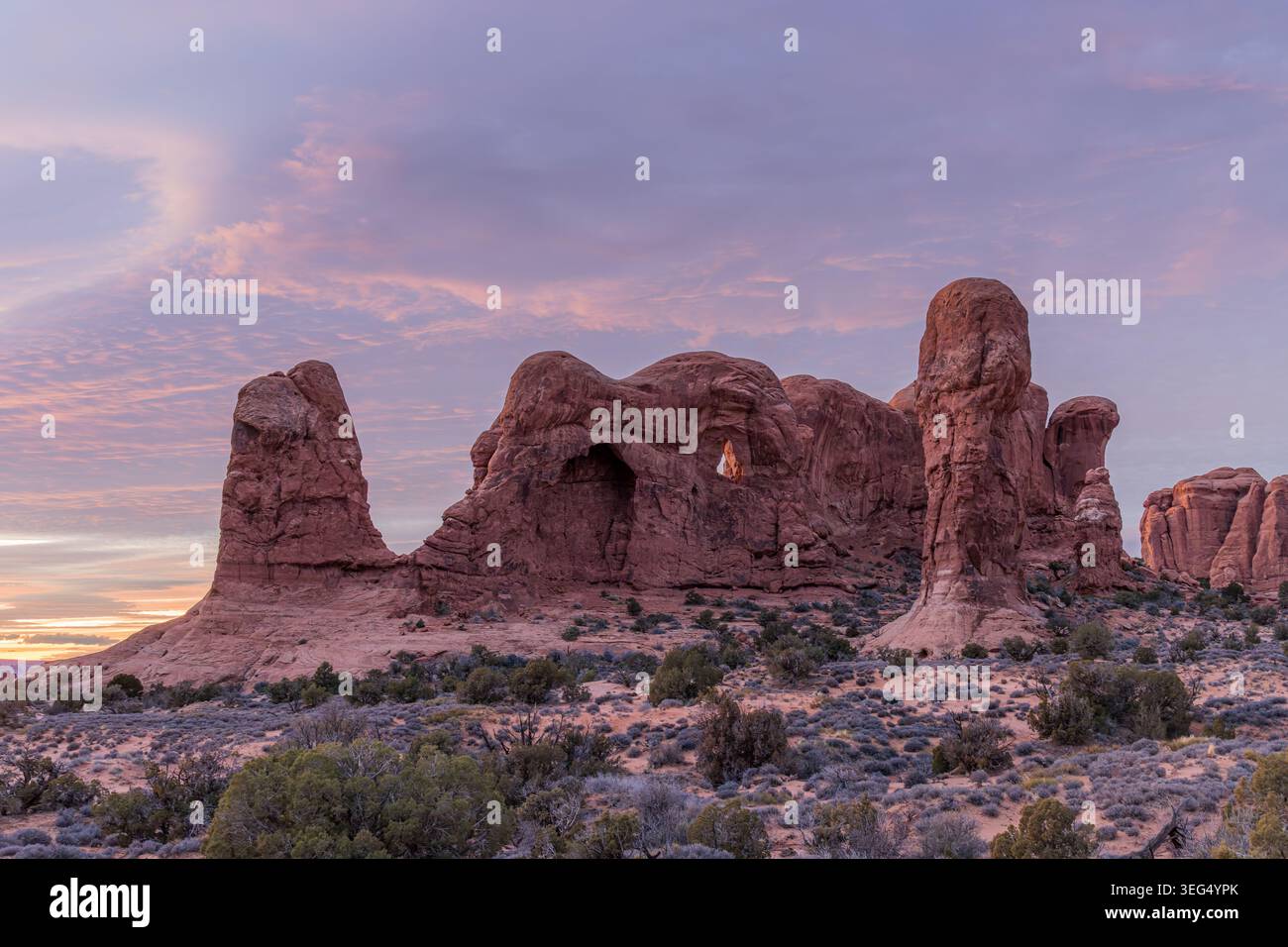 Natürliche Sandsteinbögen und hoch aufragende Felssäulen stehen während eines farbenfrohen Sonnenuntergangs in der Wüstenlandschaft. Stockfoto