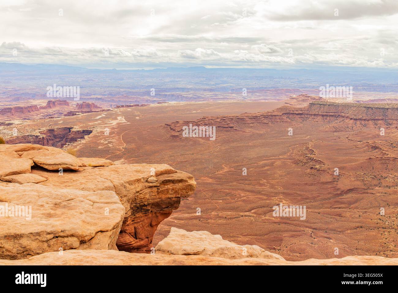 Rötliche Felsformationen überblicken ein ausgedehntes, zerklüftetes Tal mit weit entfernten mesa-Silhouetten, die im Dunst verschwinden. Stockfoto