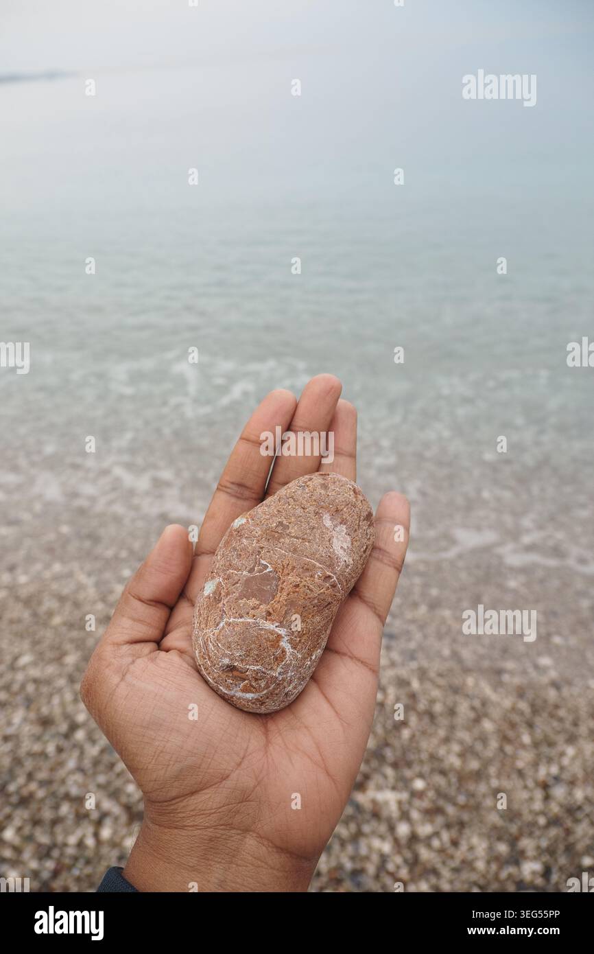 Die Person hält einen glatten Stein am Wasserrand Stockfoto