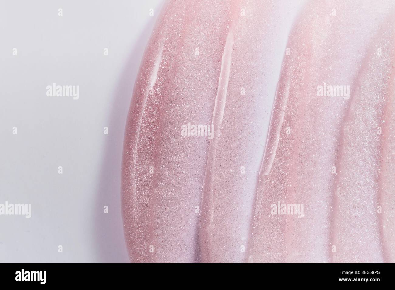 Nahaufnahme eines rosafarbenen, glitzernden Kosmetikprodukts, das strukturierte Farbfelder auf einem unkomplizierten Hintergrund erzeugt Stockfoto