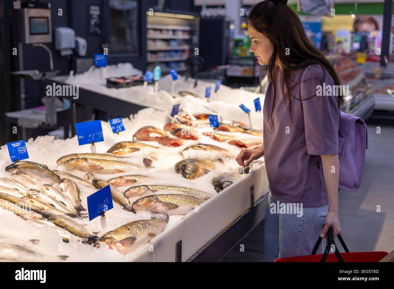 Frau, die frischen Fisch am Supermarkt aussucht. Lebensmitteleinkäufe, gesunde Ernährung, Lebensmittelauswahl und Verbraucherentscheidungskonzept. Stockfoto